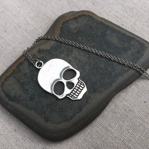 May include: A silver skull pendant necklace on a silver chain. The skull is detailed with eye sockets, a nose, and a mouth.