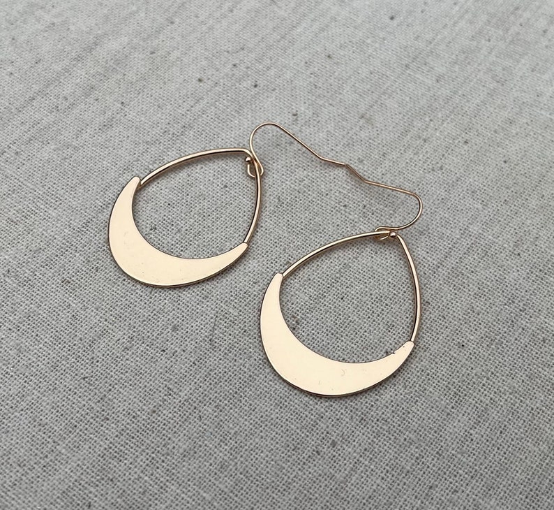 Puede incluir: Un par de pendientes de media luna de oro. Los pendientes son simples y elegantes.