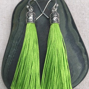 Op de afbeelding: Een paar groene kwast oorbellen met zilveren toppen. De kwasten zijn lang en zwierig, en de toppen hebben een decoratief ontwerp.
