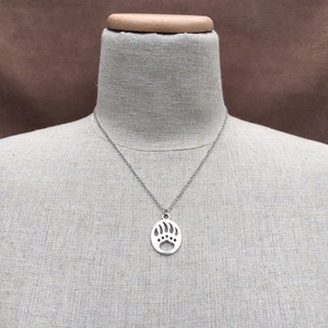 May include: A silver necklace with a bear paw pendant. The pendant is a cutout design and is on a silver chain.