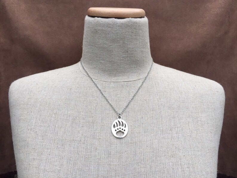 May include: A silver necklace with a bear paw pendant. The pendant is a cutout design and is on a silver chain.