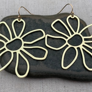 May include: A pair of gold-toned earrings shaped like stylized flowers with open centers. The earrings are dangling from a simple hook.
