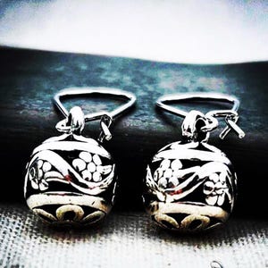 May include: A pair of silver drop earrings featuring spherical charms with an oxidized finish. Each sphere is decorated with raised floral patterns and swirling lines, suspended from simple silver ear wires that hook through the top loop.