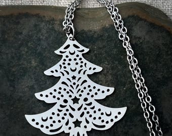 Op de afbeelding: Een zilveren ketting met een delicate, uitgesneden kerstboomhanger. De boom is versierd met sterren en manen.