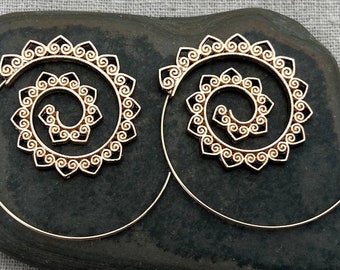 May include: A pair of gold-toned spiral hoop earrings with a delicate, intricate design. The earrings are made of thin wire and have a circular shape with a spiral pattern in the center.