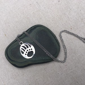 May include: A silver necklace with a bear paw pendant. The pendant is a circle with a cut-out design of a bear paw.