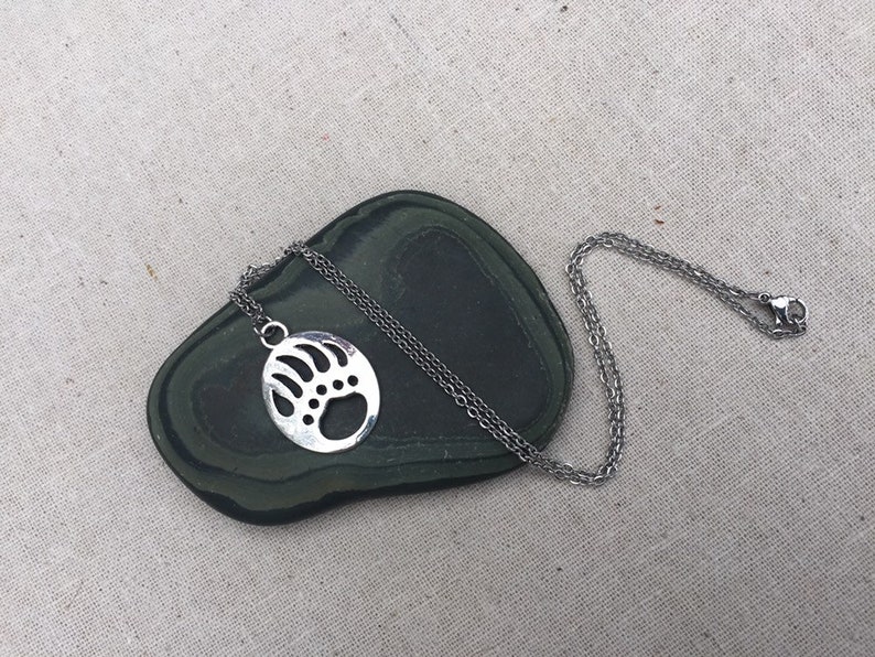 May include: A silver necklace with a bear paw pendant. The pendant is a circle with a cut-out design of a bear paw.