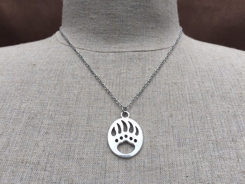 May include: A silver chain necklace with a pendant shaped like a bear paw print. The pendant is oval and has a cut-out design.