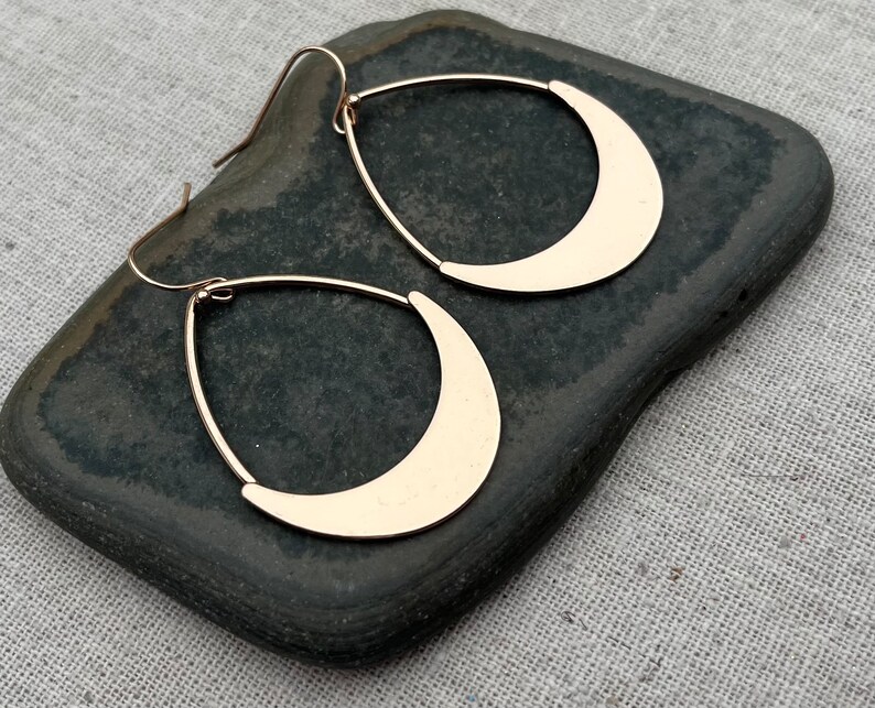 Puede incluir: Un par de pendientes de media luna de color dorado. Los pendientes son colgantes y tienen un dise&ntilde;o simple y moderno.