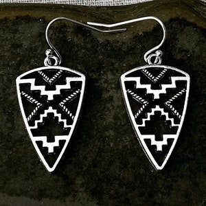 May include: A pair of silver dangle earrings with a black and white geometric pattern. The earrings are shaped like a triangle with a pointed bottom.