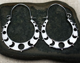 May include: A pair of silver hoop earrings with a crescent moon design. The earrings are made of metal and have a hammered finish.
