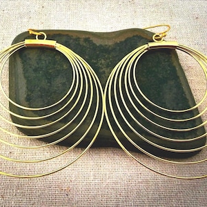 May include: A pair of gold-toned hoop earrings, each featuring five concentric circular wire rings of varying sizes that are connected at the top by a small metal bar and attached to a standard hook-style earring wire for pierced ears.