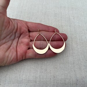 Puede incluir: Un par de pendientes de color dorado con forma de media luna. Los pendientes son colgantes y tienen un dise&ntilde;o sencillo.