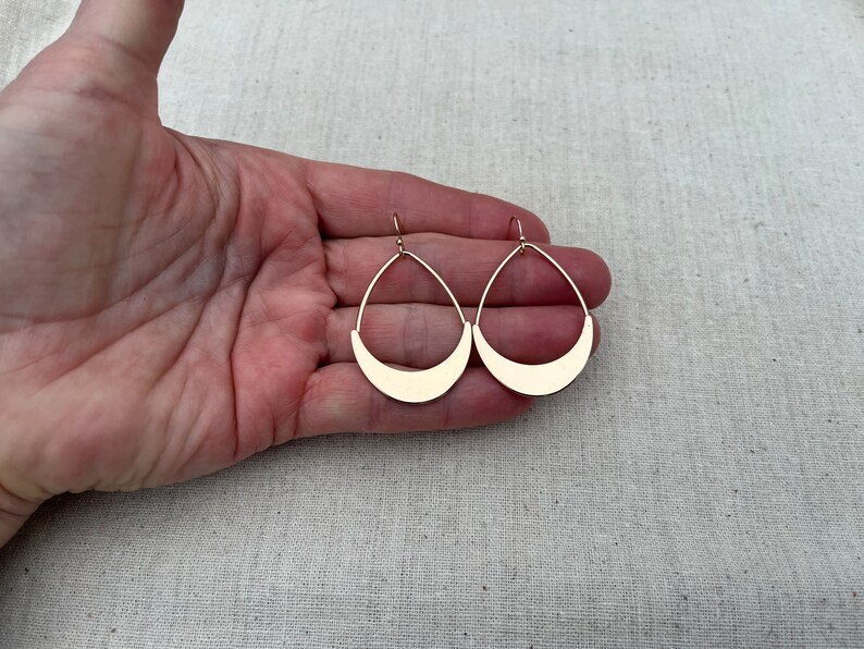 Puede incluir: Un par de pendientes de color dorado con forma de media luna. Los pendientes son colgantes y tienen un dise&ntilde;o sencillo.