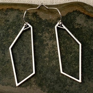 May include: A pair of silver geometric hoop earrings with a slightly irregular shape. The earrings are made of thin metal and have a simple, modern design.