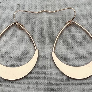 Puede incluir: Un par de pendientes de aro dorados con forma de media luna. Los pendientes son simples y elegantes.