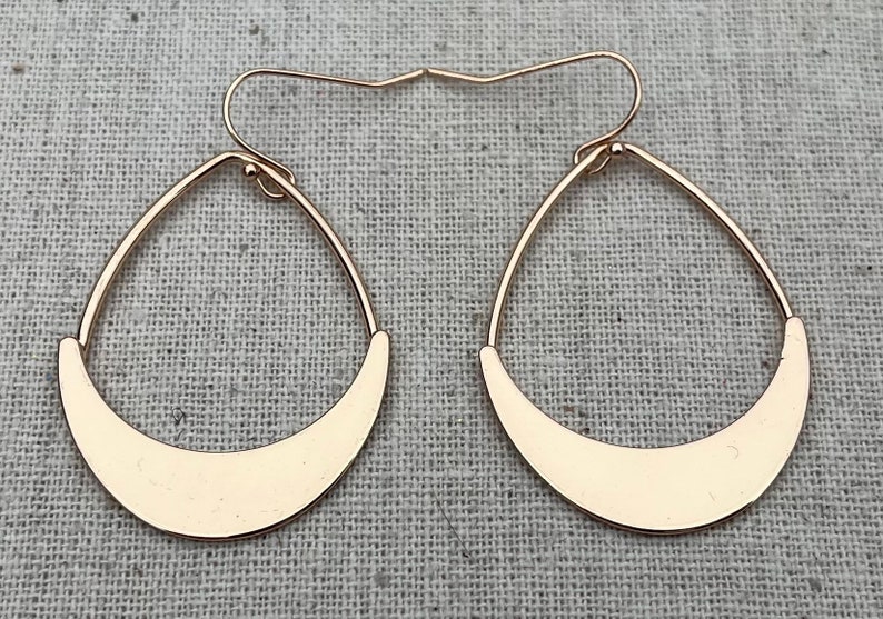 Puede incluir: Un par de pendientes de aro dorados con forma de media luna. Los pendientes son simples y elegantes.