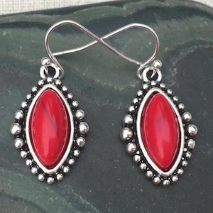 May include: A pair of silver earrings with red gemstone accents. The earrings feature a teardrop-shaped stone set in a silver bezel with a decorative border.