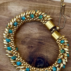 May include: Gold-coloured bracelet with turquoise stones. The bracelet features a series of gold-coloured, pointed elements, each holding a small, turquoise stone. The design is completed with a delicate chain and a clasp for adjustment.