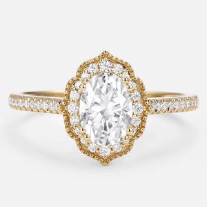 May include: A gold engagement ring with an oval-cut center stone surrounded by a halo of smaller diamonds. The band is also adorned with small diamonds. The ring has a vintage or antique style.