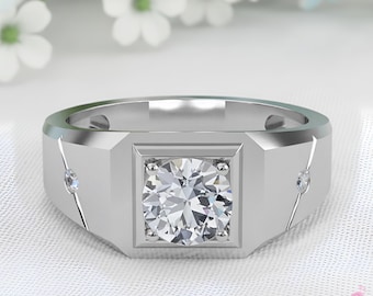 Puede incluir: Un anillo plateado con una piedra preciosa clara de corte cuadrado en el centro. El anillo tiene un diseño geométrico con pequeñas piedras de acento en los laterales. El fondo presenta flores blancas y tela blanca suave.