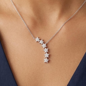 May include: A silver necklace featuring a cascade of six star-shaped pendants. The stars are adorned with small, sparkling stones. The necklace is displayed against a dark blue background.