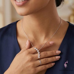 May include: A silver necklace with a cascade of five star-shaped pendants, each encrusted with small, sparkling stones. The necklace is worn with a matching ring. The model is wearing a dark blue top.