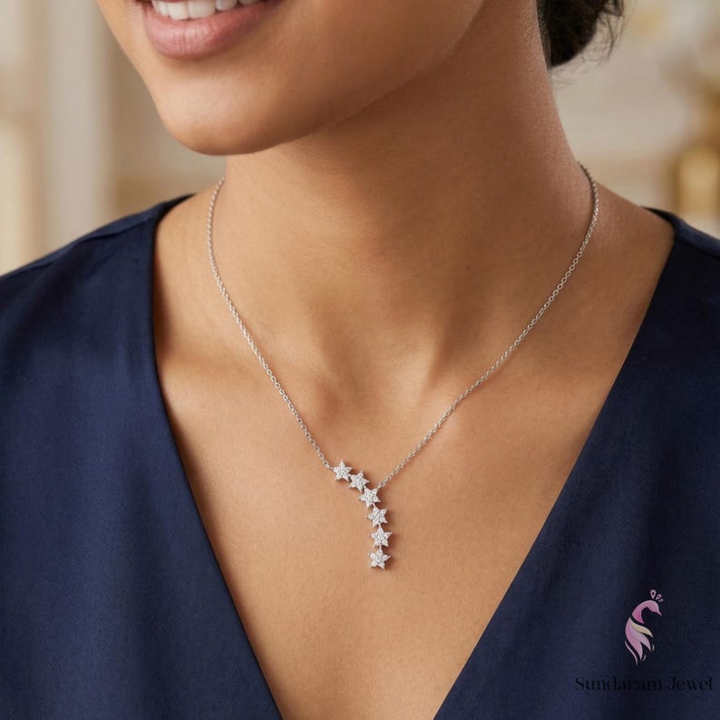 May include: A silver necklace featuring a cascade of six star-shaped pendants. The stars are adorned with small, sparkling stones. The necklace is displayed against a dark blue background.