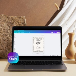 May include: A laptop displays a digital invitation with the text "A Chapter to Remember" and "Emily's Anniversary". The design features floral elements and a decorative border. The laptop is on a light-colored surface.