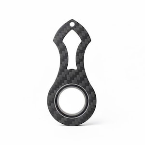 May include: A black carbon fiber tool with a unique shape. It features a key ring hole at the top, a central cutout, and a circular opening at the bottom. The tool has a textured, woven pattern throughout.
