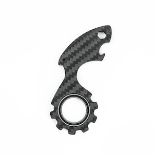 May include: A black and gray multi-tool with a carbon fiber weave pattern. The tool features a bottle opener, a gear-shaped design, and a hexagonal socket. The tool is designed for various uses.