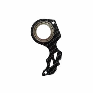 Könnte beinhalten: Ein schwarzer Lagerhalter aus Kohlefaser mit einem silbernen Lager in der Mitte. Der Halter hat eine einzigartige Form mit ausgeschnittenen Designs und einer strukturierten Oberfläche. Der Artikel ist für mechanische Anwendungen konzipiert.