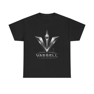 Pode incluir: Uma t-shirt preta de manga curta com um gráfico prateado metálico de uma letra V grande com uma bola de basquete acima. Abaixo do V, o texto diz VASSELL e SAN ANTONIO numa fonte estilizada, com a silhueta ténue de uma linha do horizonte.