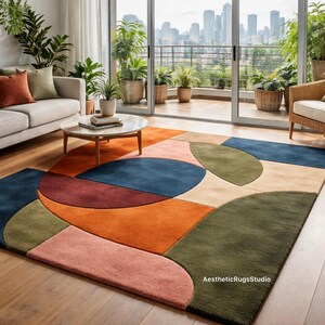 Könnte beinhalten: Moderner Teppich mit geometrischem Muster in einem Wohnzimmer. Der Teppich zeigt Formen in Blau, Orange, Grün und Rosa. Er liegt auf einem Holzboden, im Hintergrund sind ein Sofa und ein Sessel zu sehen.