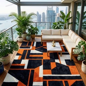 Könnte beinhalten: Ein moderner Outdoor-Teppich mit geometrischem Design in Schwarz, Orange und Weiß. Der rechteckige Teppich bedeckt eine Holzterrasse, mit einem Sofa und Topfpflanzen im Hintergrund. Der Teppich misst ca. 244 x 305 cm.
