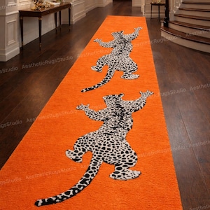 Puede incluir: Una alfombra de pasillo naranja con dos diseños de leopardo en blanco y negro. La alfombra es rectangular y está colocada en un pasillo con suelo de madera oscura. Los diseños de leopardo están orientados en direcciones opuestas.
