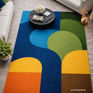 Könnte beinhalten: Rechteckiger Teppich mit geometrischem Design. Der Teppich hat Abschnitte in Blau, Grün, Gelb, Orange und Braun. Das Design umfasst geschwungene und rechteckige Formen. Der Teppich liegt auf einem grauen Fliesenboden.