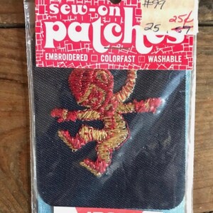 May include: A vintage sew-on patch featuring an embroidered figure in red and gold thread. The patch is on a navy blue background and is packaged in a clear plastic sleeve. The packaging includes the words "Sew-on patches", "Embroidered", "Colorfast", "Washable", and "Iron On".