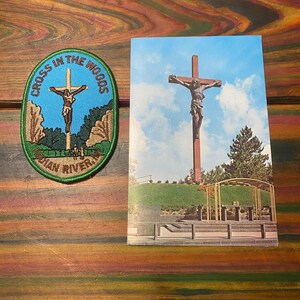 May include: An embroidered patch and a postcard featuring the Cross in the Woods. The patch has a blue background with a depiction of Jesus on the cross. The postcard shows a large wooden cross with a figure of Jesus.