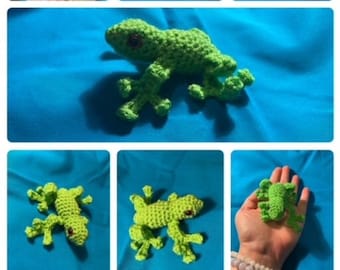May include: A green crocheted gecko toy with black eyes. The gecko is posed on its four legs with its tail curled up. The gecko is about 4 inches long.