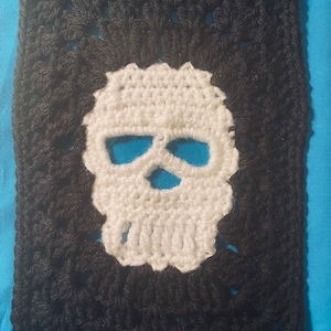 May include: A black and white crocheted square with a white skull design in the center.