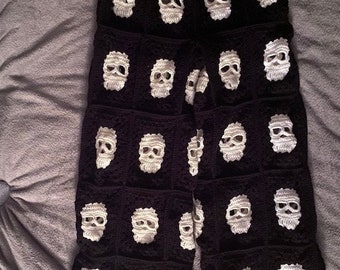 May include: Black crochet pants with a white skull pattern. The pants have a drawstring waist and a wide leg.
