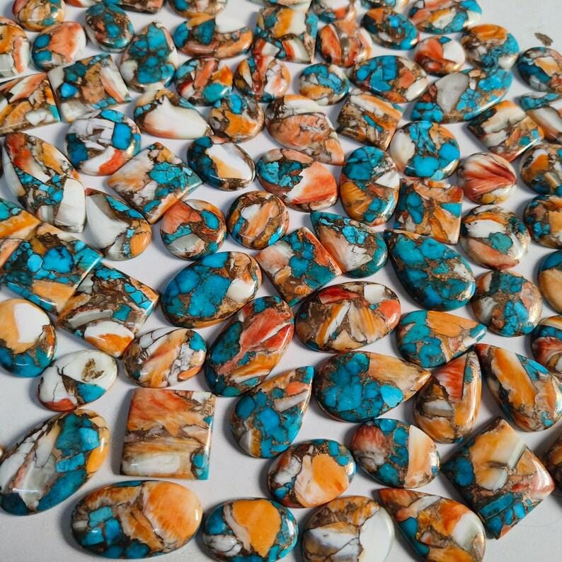 May include: A collection of polished gemstones in various shapes, including ovals, squares, and teardrops. The stones feature a striking combination of turquoise blue, orange, and white hues, with intricate patterns and textures. These gemstones are ideal for jewelry making.