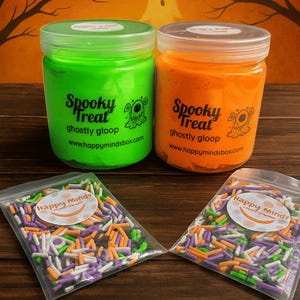 May include: Two jars of green and orange "ghostly gloop" with the text "Spooky Treat" and a monster graphic. Below are two small bags of colorful sprinkles with the text "Happy Minds". The background is a Halloween-themed design.