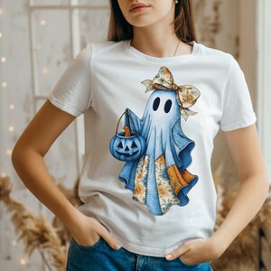Op de afbeelding: Wit T-shirt met een Halloween-geestontwerp. De lichtblauwe geest draagt een bloemenstrik en houdt een blauwe pompoenemmer vast. Bloemenstof patches sieren de geest en creëren een unieke, feestelijke uitstraling.