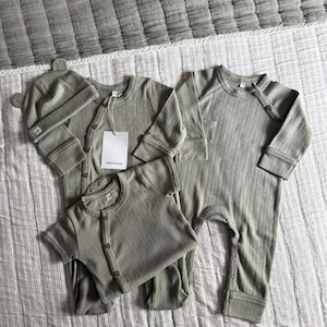 May include: A set of three ceramic mugs with a speckled, matte finish. The mugs are in shades of cream, light grey, and dark grey. Each mug has a simple, minimalist design, ideal for coffee or tea.