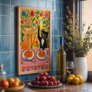 May include: A framed art print featuring two cartoon cats enjoying spaghetti. One cat is orange, the other is black. The background is yellow with colorful flowers. The print is in a light wood frame, displayed on a blue tiled wall.