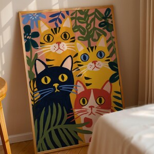 May include: A framed art print featuring four stylized cats in a colorful, whimsical design. The cats are yellow, orange, red, and black, surrounded by green foliage and blue flowers against a pink background. The artwork is in a wooden frame.