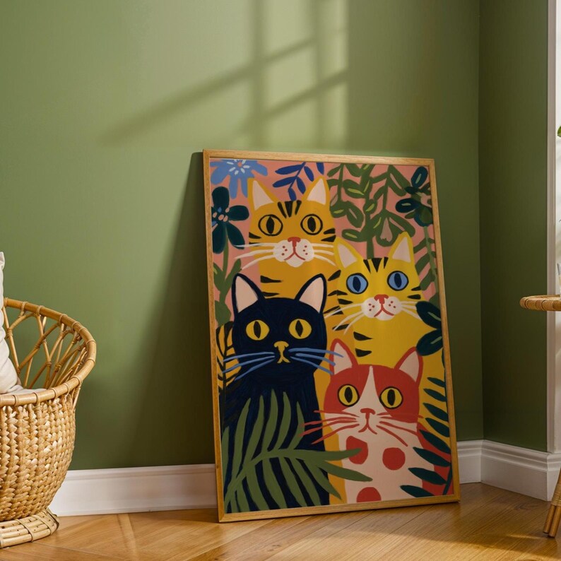 May include: A framed art print featuring four stylized cats with vibrant colors. The cats are yellow, orange, red, and black, surrounded by green leaves and blue flowers against a pink background. The frame is a light brown color.
