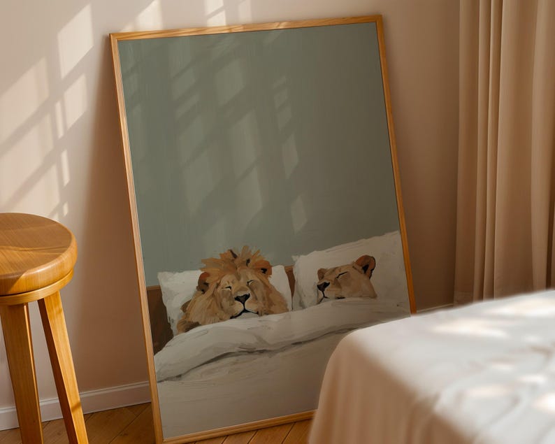 May include: A framed print depicts two lions resting in a bed. The artwork shows a male lion and a lioness lying on pillows under a white duvet. The frame is made of light-colored wood.